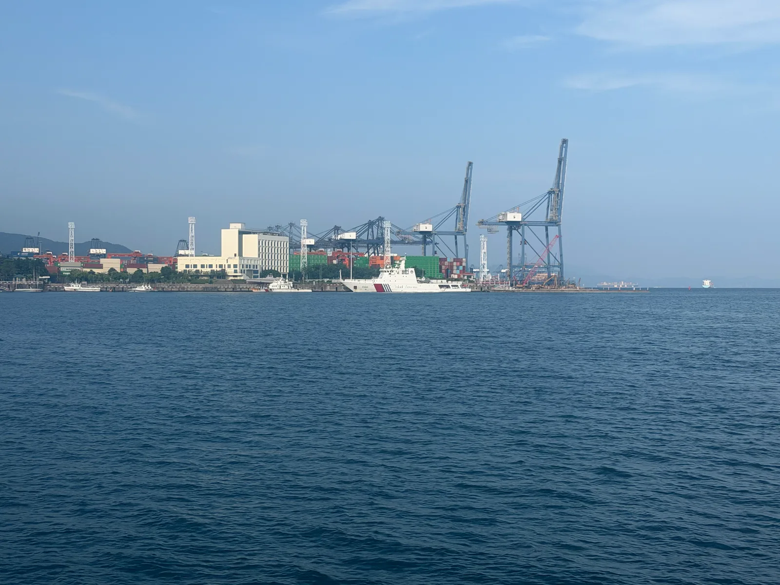 隔着蓝色海面望向港口吊机与白色船只